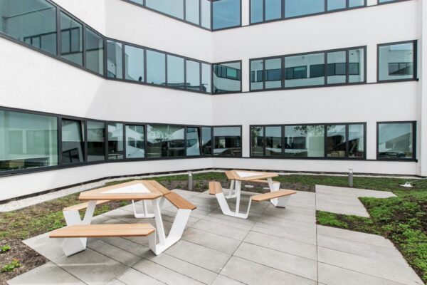 Binnenplaats van een modern kantoorgebouw aan de Grote Marktstraat met twee houten picknicktafels op een betegeld terras.